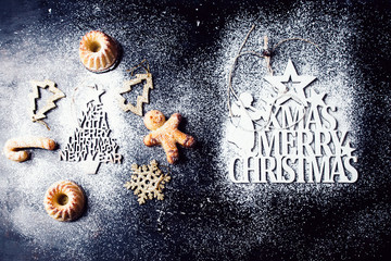 Obraz na płótnie Canvas Christmas mini bundt cake and decoration on a black board with icing sugar and stenciled christmas greetings,top view, flat lay