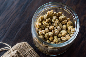 Jar of Dried Mulberries on Dark Wooden Surface.
