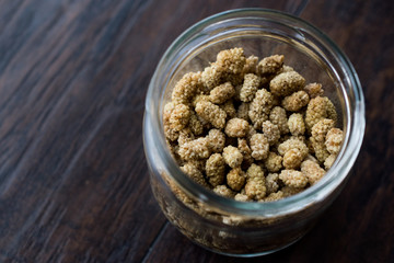 Jar of Dried Mulberries on Dark Wooden Surface.