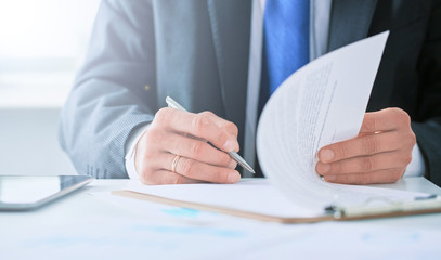 Businessman in dark suit sitting at office desk signing a contract with shallow focus on signature.