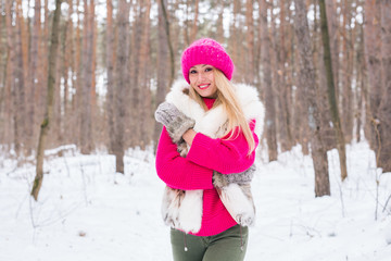 Fototapeta na wymiar Beauty, fashion and people concept - Attractive blond woman standing in pink hat and sweaters in winter wood and smiling