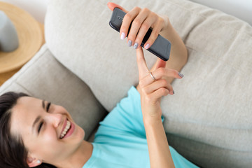 laughing woman laying on the couch using phone. idle lifestyle and mobile devices addiction.