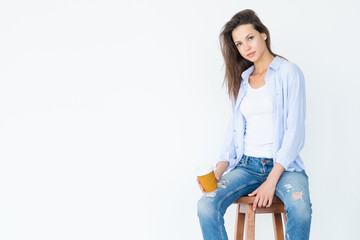 casual woman sitting on a stool holding coffee cup on white background.