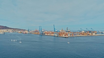 Naklejka premium aerial drone image of the harbor with numerous containers piled up next to cranes ans a small sailing dinghy race