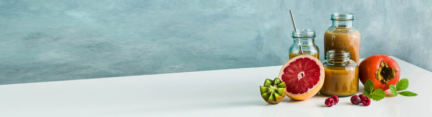 different glasses with freshly made grapefruit, kiwi, persimmon and raspberry smoothies. on white table and blue background. healthy food. morning breakfast