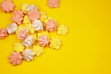 Multi-colored mini-meringues on a yellow background, top view. Place for text.