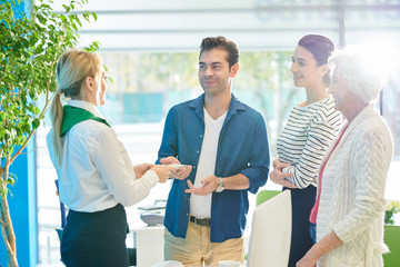 Happy family including grandmother standing in modern light office of bank and talking to...