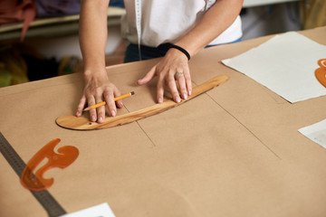 Working place in design studio. Female designer drawing flat paper patterns using measuring tape...