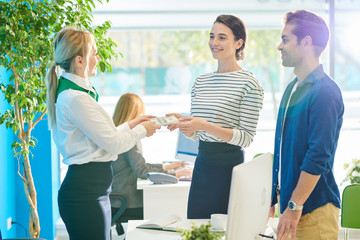 Obraz premium Positive satisfied young couple in casual clothing standing in modern bank and receiving stack of dollar banknotes while exchanging money for travelling