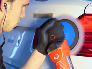 The professional guy (man) with headphones and a working uniform polishes the car body with a polishing tool. Concept from: Master class, Car Refreshment, Garage service, Special tools.
