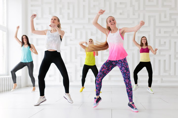 Group of young women dancing with arms raised while having a fitness dance class
