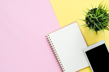 Office desk working space - Flat lay top view photo of working space with blank mock up tablet, plant tree and notebook on pastel background. Pastel pink yellow color copy space working desk concept.