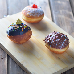 Close up view of tasty various donuts on wood background. Hanukkah celebration concept. Round jelly or jam doughnut sufganiyot and chocolate sufganiyah for Chanukah Jewish holiday.