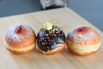 Close up view of three tasty various donuts on wood background. Hanukkah celebration concept. Round jelly or jam doughnut sufganiyot and chocolate sufganiyah for Chanukah Jewish holiday.