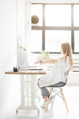 Young business woman working at home behind a laptop and stretching her hands. Creative Scandinavian style workspace