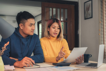 Young asian couple managing finances, reviewing their bank accounts using laptop computer and calculator at modern home. Woman and man doing paperwork together, paying taxes online on notebook pc.