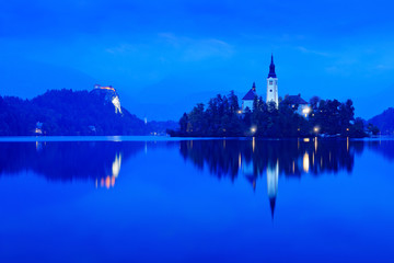 Autumn landscape on the lake. Green tree leaves in foreground. Twilight evening light in, Bled, Slovenia.  lake island, St Martin Catholic church and Castle with mountain Range, Slovenia, Europe.