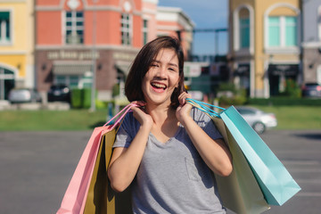 Naklejka premium Happy young Asian woman shopping an outdoor market with background of pastel buildings and blue sky. Young asian woman smile with a colorful bag in her hand. Outdoor woman lifestyle shopping concept.