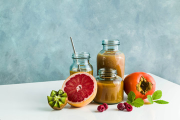 different glasses with freshly made grapefruit, kiwi, persimmon and raspberry smoothies. on white table and blue background. healthy food. morning breakfast