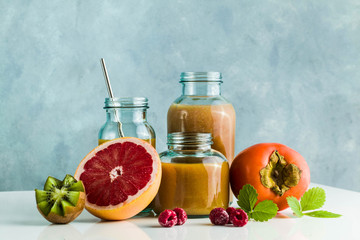 different glasses with freshly made grapefruit, kiwi, persimmon and raspberry smoothies. on white table and blue background. healthy food. morning breakfast