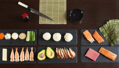 Preparing rolling sushi. Ingredients on the black stone plates with knife, bamboo mat and bowl....