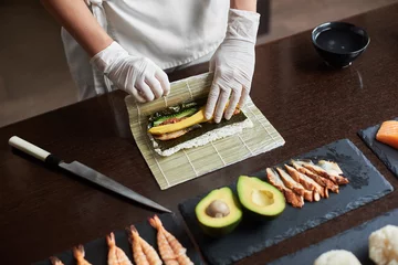 Papier Peint photo Bar à sushi Le maître prépare un rouleau de sushi avec du nori, du riz, du concombre, de l& 39 anguille et de l& 39 omelette à l& 39 aide d& 39 un tapis de bambou. Vue rapprochée du processus de cuisson des sushis