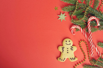 Christmas composition. The composition includes gingerbread cookies in the shape of a little man, caramel canes, fir branches, beads. View from above. Red background. Space under the text.