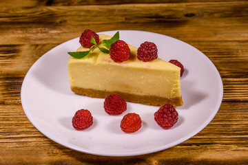 White plate with cheesecake New York, leaf of mint and raspberries on wooden table
