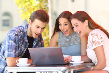 Surprised friends watching media on laptop in a coffee shop