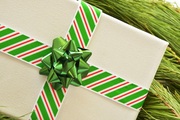 Fototapeta premium Close up overhead of white canvas wrapped as Christmas gift or present, with striped ried, green, and white ribbon, and green bow,, on pine needle background. Studio shot.