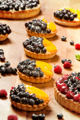 Sweet tarts with fruits, raspberries, blueberries and peaches on a wooden background