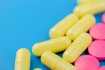 Pink pills and yellow medicine on a blue background. Cocept treatment selection. Close up.