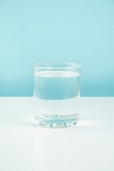 Glass with water on a table. Hunger or diet concept: clean transparrent drink in white and blue background