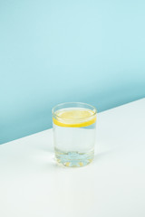 Glass with lemon water on a table. Hunger or diet concept: Light tonic drink in white and blue background