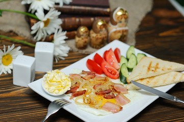 breakfast - bread and butter on a background of scrambled eggs and bacon with tomatoes and cucumbers on a wooden background close-up