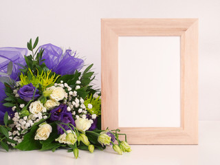 Flower bouquet and blank photo frame on table in front of the wall