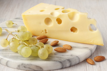 Maasdam cheese, grapes and almonds on a marble board.