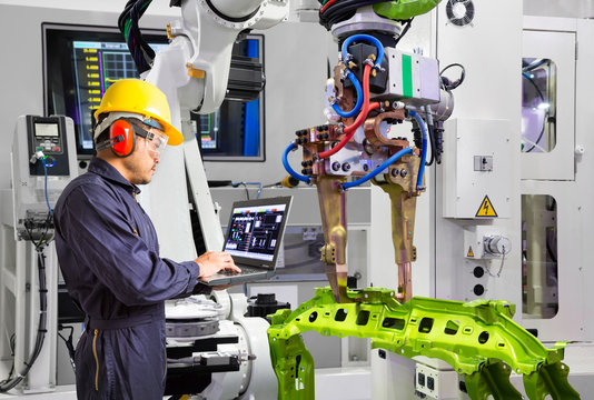 Maintenance engineer using laptop computer control robot grip automotive workpiece in smart factory, Industry 4.0 concept