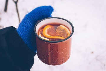 Mulled wine in a red cup in women's hands in mittens. Hot winter drink outdoor in snowy winter...