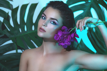 Young and beautiful woman with perfect smooth skin is holding orchid flowers