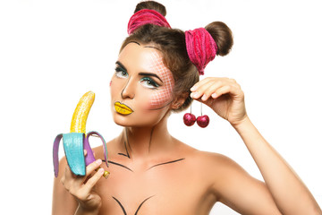 Beautiful model with creative pop art makeup holding banana and cherries
