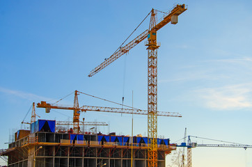 Fototapeta na wymiar Building of a residential house, working cranes on a background of blue sky.