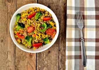 View from above of bowl with tuna risotto with vegetables, tomatoes, broccoli and parsley, brown...