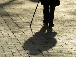 Silhouette of man walking with a cane, long shadow on pavement. Concept of blind person, disability, old age, diseases of the spine