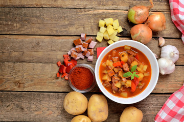 View from above of potato and sausage goulash, pepper, onion and garlic on wooden table