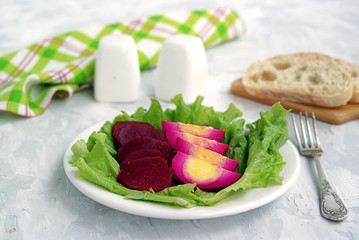 White plate with appetizers, pickled eggs and spicy beets on green salad leaves. Served with fresh wheat bread.