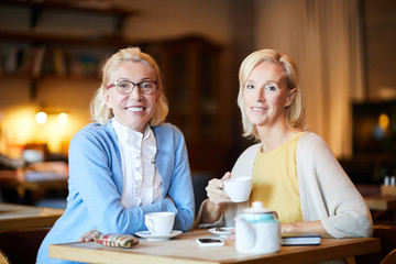 Two mature females in smart casual looking at you while spending time in cafe