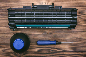 Laser printer cartridge, screwdriver and bottles with toner on the table. Office equipment...