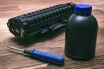 Laser printer cartridge, screwdriver and bottles with toner on the table. Office equipment...