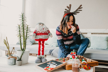 .Sweet and cheerful woman enjoying christmas at her home. Wearing christmas costume and eating...